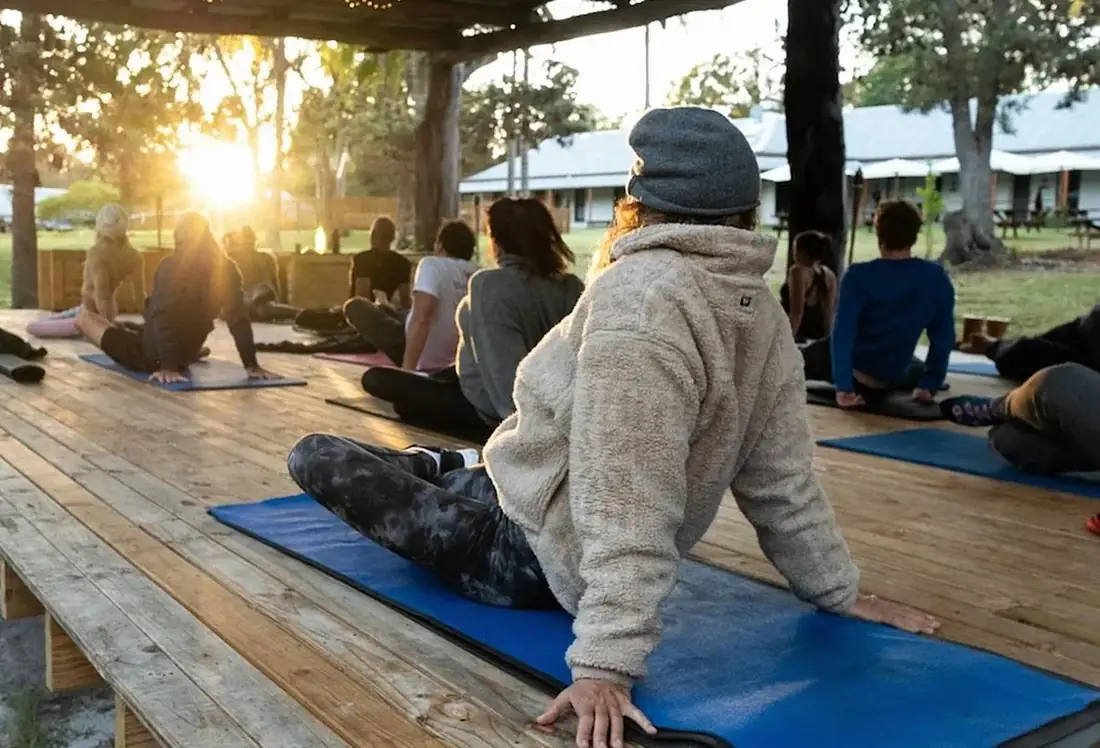 Group sitting and stretching on mats outdoors at sunrise